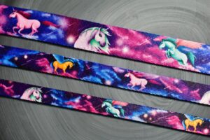 Zdjęcie przedstawia trzy taśmy materiałowe, z których powstają smycze dla psów. Każda taśma ma inną szerokość. Są w kolorach: niebieskim, fioletowym, różowym i przedstawiają jednorożce.