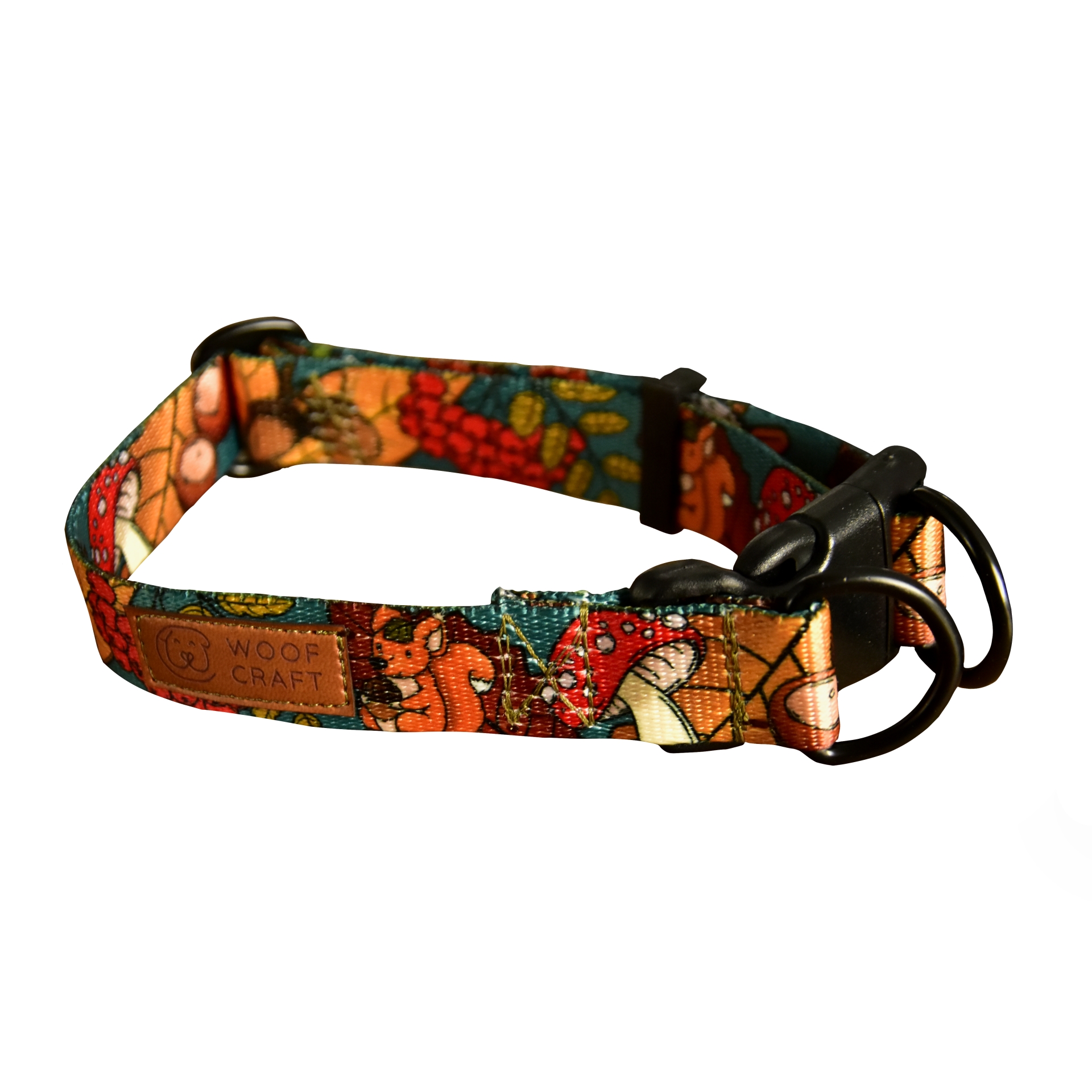 Zdjęcie przedstawia obrożę z zapięciem typu double lock. Taśma ma ciepłe barwy i wzór z motywem jesieni: liści, grzybów, wiewiórek i jeży.